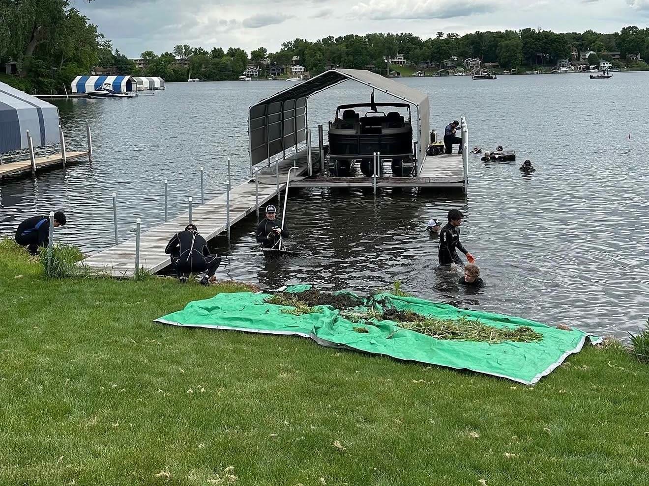 Scuba Weed Control dive crew hand-pulling lake weeds at a dock